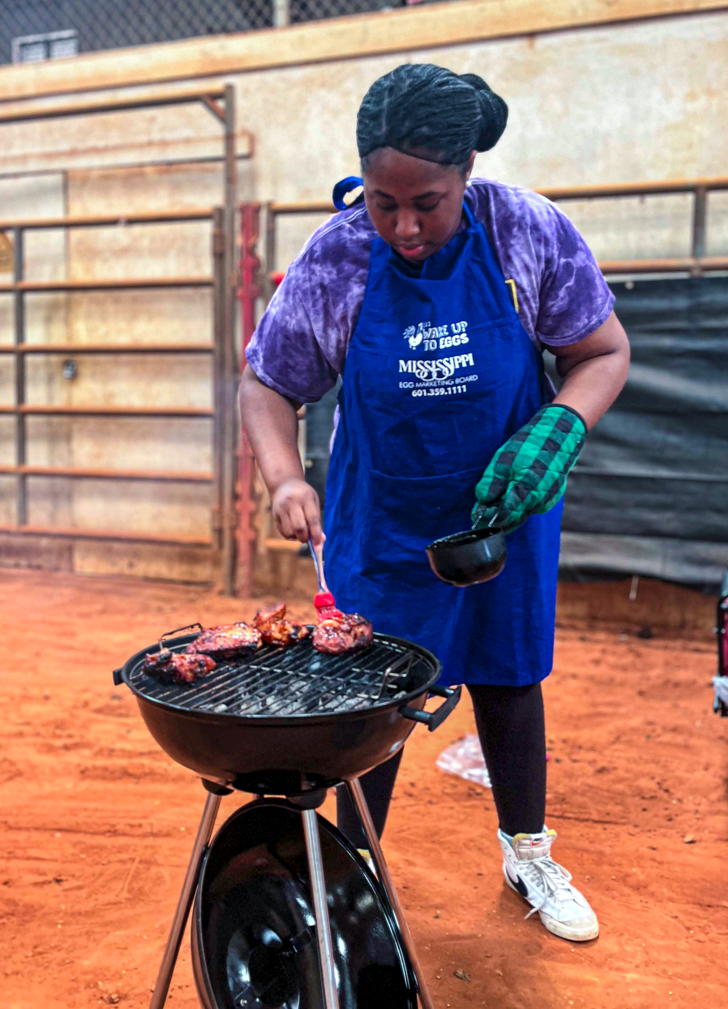 A contestant is putting sauce on chicken cooking over a hot grill.